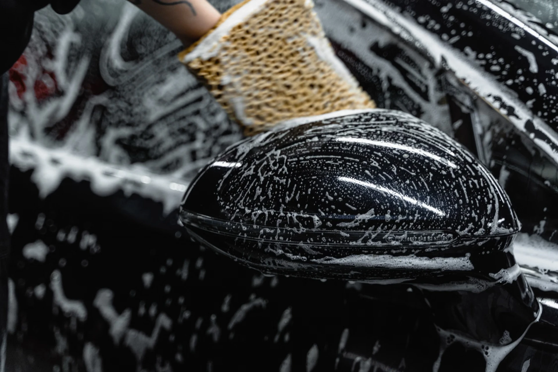 Wash mitt and foam lifting dirt from a black car's side panel during an exterior detail